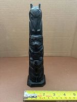 Front view of entire totem pole beside ruler showing overall form and height