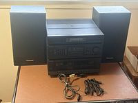 Full view of Panasonic stereo main unit flanked by two matching speakers with cables in front