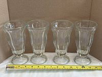 Four clear glass parfait glasses side by side with ruler