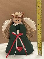 Front view of wooden angel with measuring tape showing height, green dress, red bow, heart applique