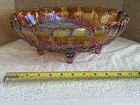 Side view of iridescent oval footed bowl with tape measure indicating length ~13.5 in