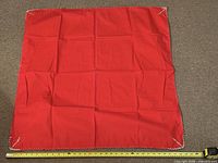 Full view of square red tablecloth with measuring tape indicating roughly 36" width, showing overall condition