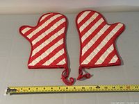 pair of candy cane striped oven mitts with measuring tape for scale