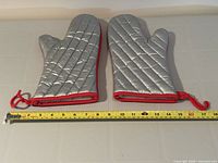 Top view showing silver quilted side of both mitts next to measuring tape