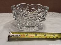 Front view of clear cut glass candy dish on three feet with tape measure showing width ~5 inches