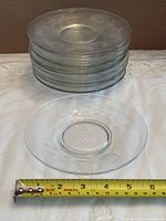 Stack of 11 clear glass plates with measuring tape showing roughly 6-inch diameter
