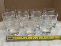Front view showing all 11 etched cornflower cocktail glasses with tape measure for scale