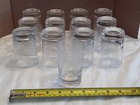 Group of juice glasses upside down with one upright, tape measure shows length