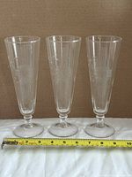 Three stemmed etched pilsner glasses side by side with tape for scale