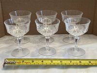 Front view of six etched crystal liqueur glasses aligned in row with tape measure for scale