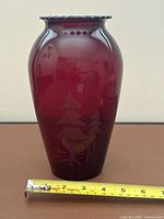 Full view of cranberry etched glass vase with measuring tape showing height