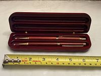 Open wooden case displaying pen and pencil with measuring tape indicating size