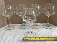Five clear fishbowl wine glasses aligned with tape measure showing scale