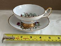 Cup on saucer beside tape measure showing ~5.5 in saucer diameter