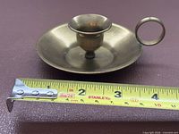 Brass candle holder beside measuring tape showing diameter