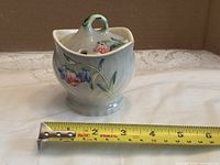 Creamer with lid beside tape showing width