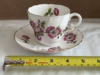 Side view of teacup on saucer with tape measure showing diameter