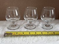 front view of three matching clear glass snifters with tape measure