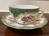 Teacup on saucer showing green fish-scale border and floral painting