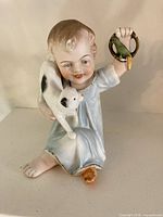 Full view of seated child figurine holding cat and parrot