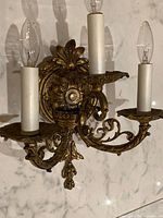 Full view of three-arm gilt brass wall sconce mounted on marble backdrop