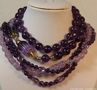 Amethyst beaded necklace coiled to show gold clasp and barrel bead