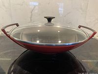 Wok with glass lid on stovetop, side profile showing handles and lid