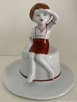 Full view of porcelain boy figurine seated on hat