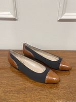 Pair of flats side view showing black fabric uppers and brown leather cap toe and heel