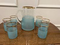 Front view of pitcher and glasses showing blue frosting and gold rims