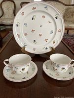 Full set displayed: dinner plate on stand behind two teacups with saucers