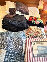 All blankets and pillows laid on bed including packaged comforter set, patterned comforter, faux fur throw and four pillows