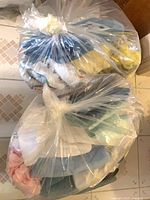 Two clear plastic bags stuffed with mixed clothing and towels on tiled floor