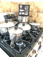 Overall view of five pots with lids on stovetop plus boxed item