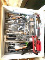 Drawer tray filled with mixed stainless steel flatware and utensils