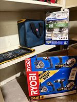 Shelf with Ryobi tool kit box, Dremel accessory set, tool bag, and rolled-out drill bit pouch