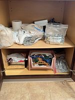 Cabinet shelves showing fabrics, cord spool, plastic tray of cords/beads, bags of drapery hooks