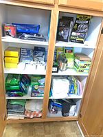 Open cabinet showing dish towels, cleaning cloth packs, Alien Tape boxes, plastic hangers and other supplies