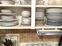 Cupboard section showing multiple stacks of white ceramic plates and bowls on wire shelf organisers