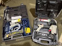 Both brad nailers open in their carry cases with cords, nails and accessories visible