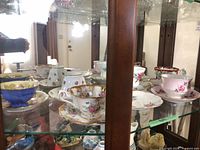 Multiple floral bone-china teacups and saucers displayed in glass cabinet