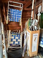 Stack of aluminum folding beach chairs, two hung chairs, striped umbrellas and poles against wall