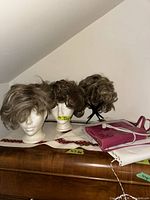 three wigs on stands, pink purse on dresser