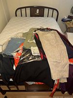 Stack of various garments on bed showing blazer, trousers, packaged blouses and floral robe-style top