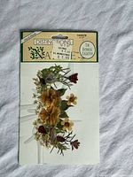 Front view of sealed pressed botanical adhesive sheet showing pansies and assorted flowers