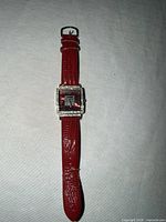 Full watch showing red strap and square case