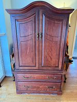 Front view of cherry armoire cabinet showing double doors, two drawers, crown top