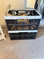 Two stacked black plastic collapsible crates containing assorted wooden and metal hangers