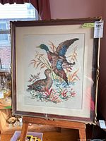 Full view of framed cross-stitch artwork on easel