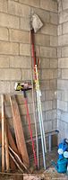 Group of poles, fruit picker, tubing, rope leaning against wall
